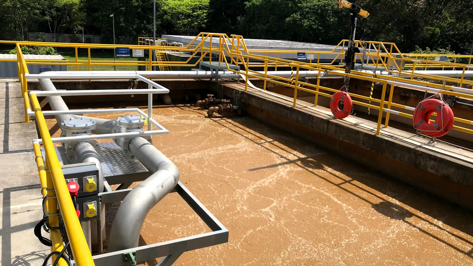 Tanque de aeração em operação numa estação de tratamento de efluentes, com passarelas e guarda-corpos de segurança